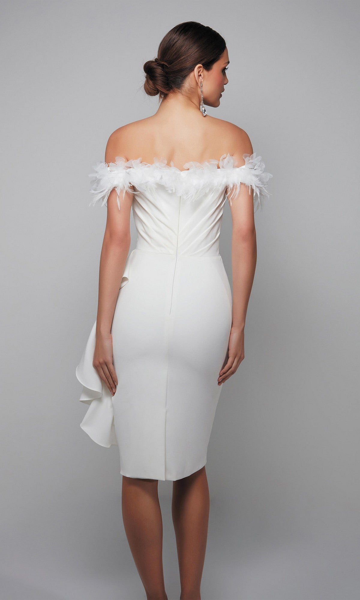 A woman in the Alyce 70000 knee length semi-formal dress, featuring off-the-shoulder white fabric with feather trim, stands facing away with her hair in a low bun.